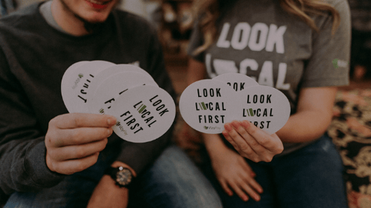 people-holding-look-local-first-stickers